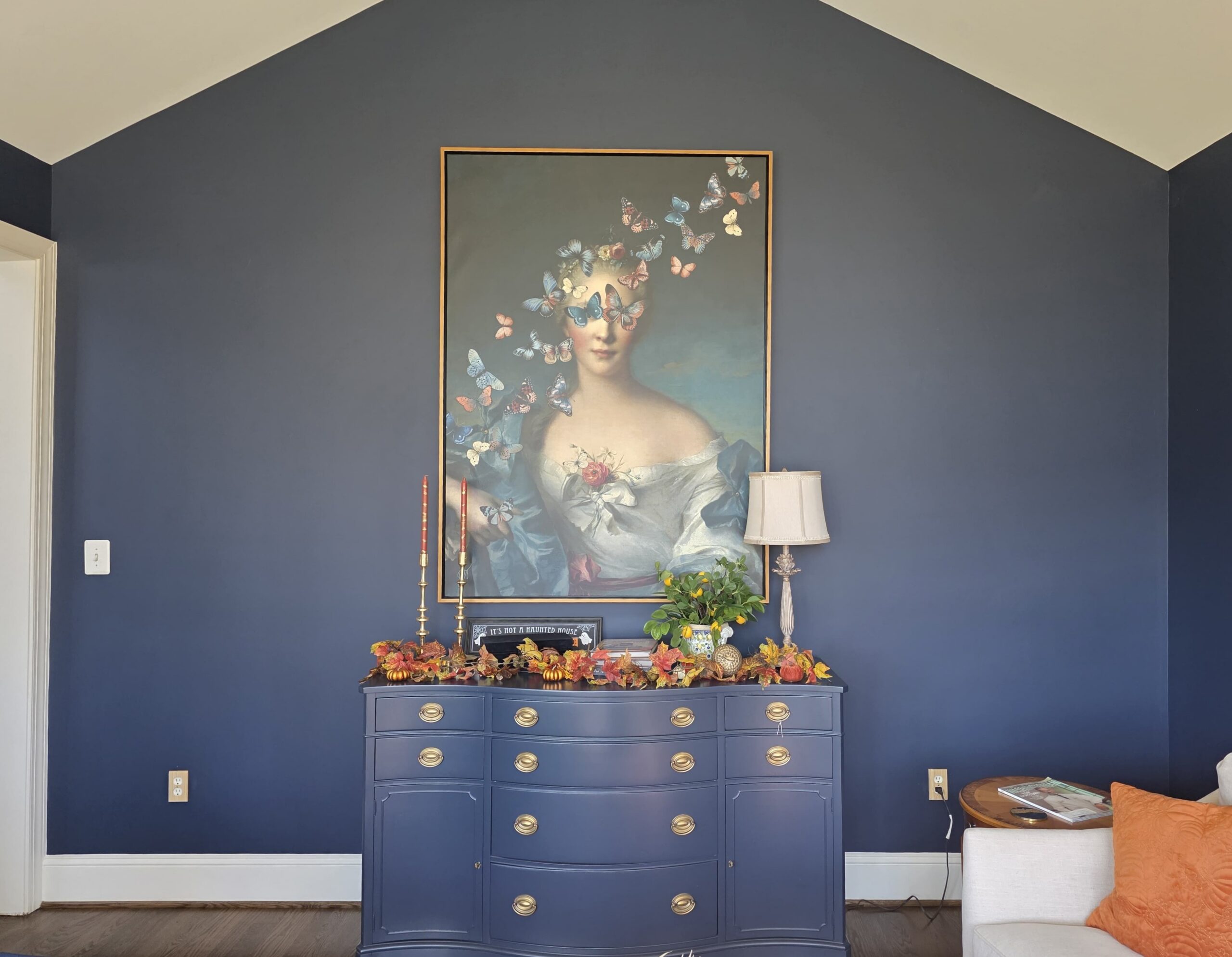 A beautifully painted dark blue accent wall in a living room with a vaulted ceiling and decorative console.