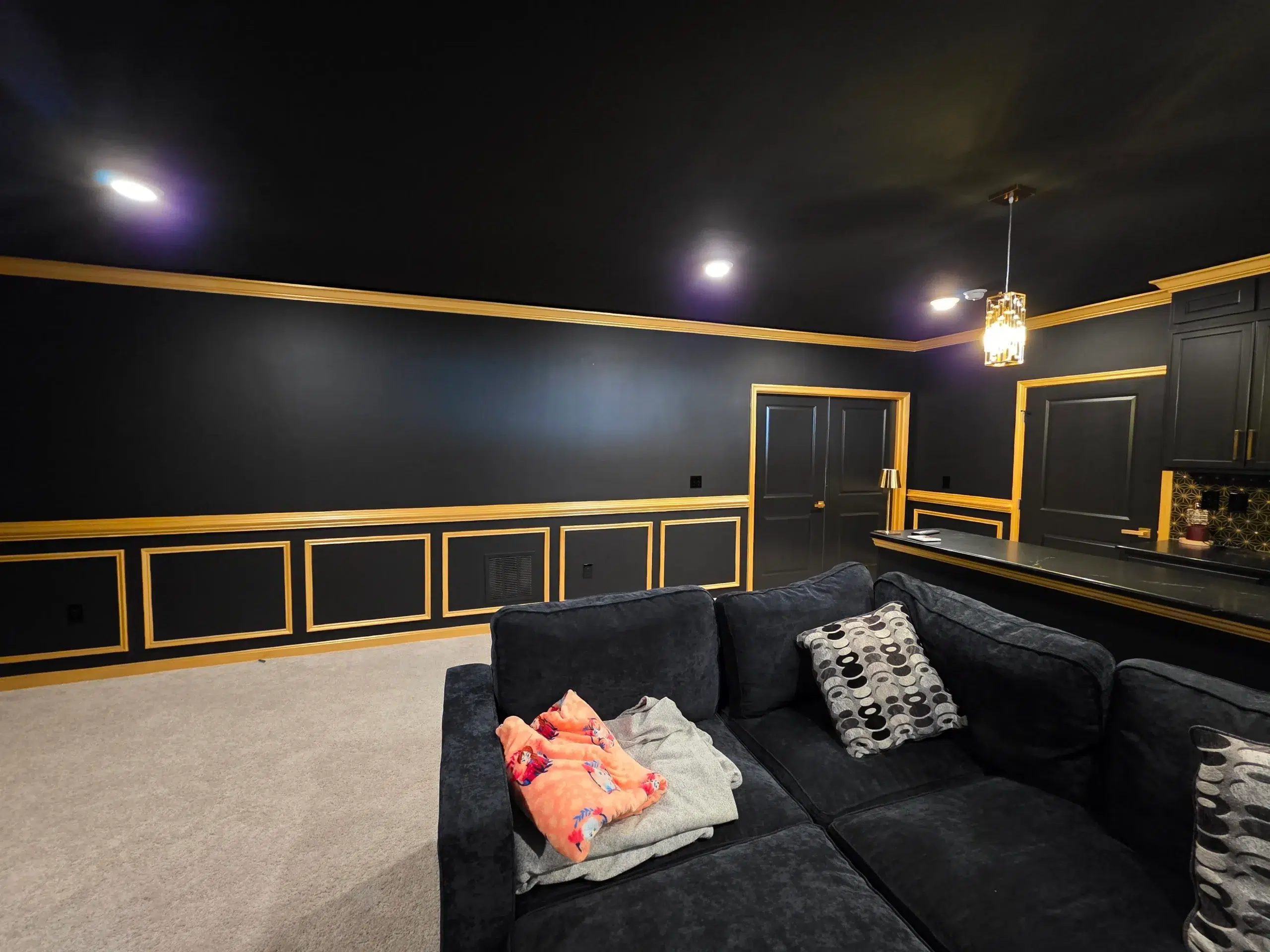 Modern Basement Entertainment Room Painting with Black and Gold Accents A newly painted basement entertainment room featuring black walls, gold wainscoting, and a comfortable sofa.