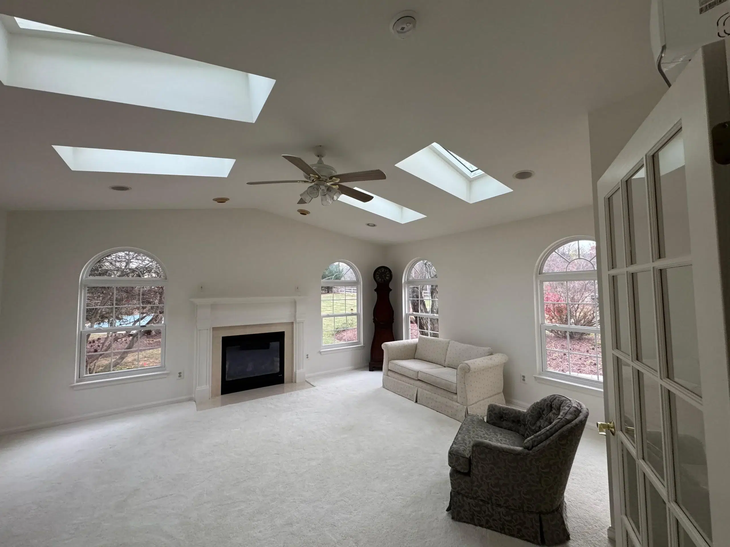 Bright White Living Room Interior Painting Project A spacious living room with freshly painted white walls, a fireplace, and multiple windows and skylights.