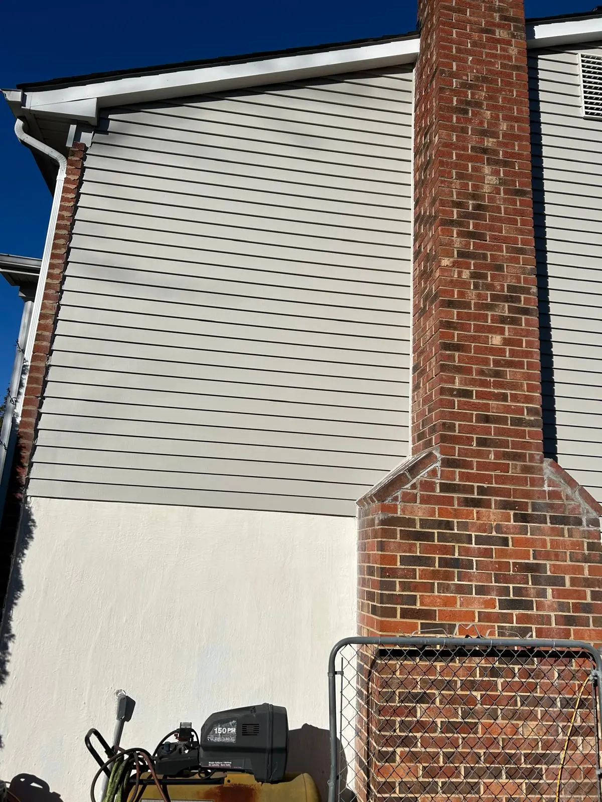 Exterior House Painting with Siding and Stucco Foundation Side of a house with light gray siding, a brick chimney, and a freshly painted white stucco foundation.