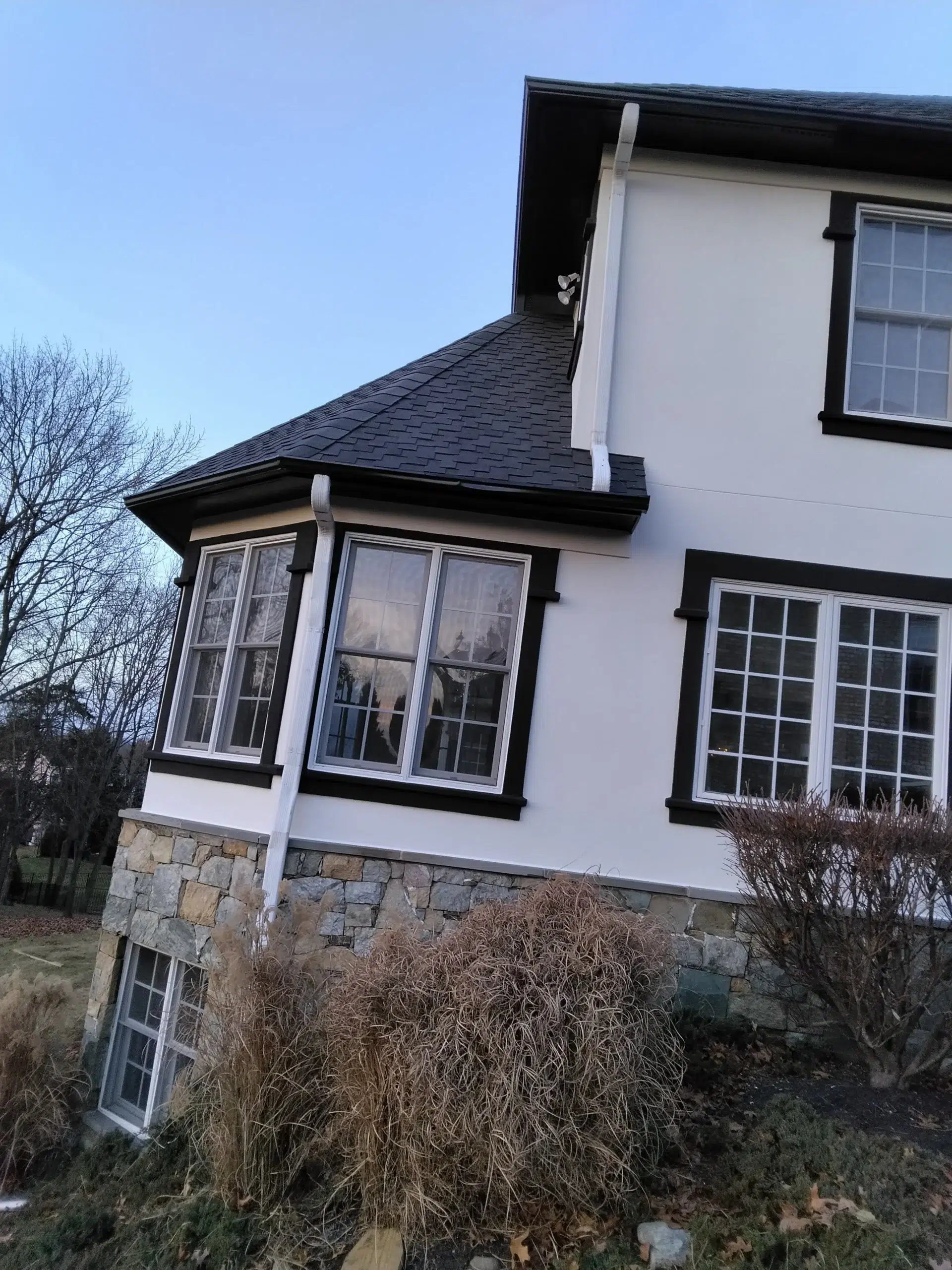Luxurious Basement Bar Painting with Black Walls and Gold Trim A beautiful white house exterior with striking black window trim and a natural stone foundation.