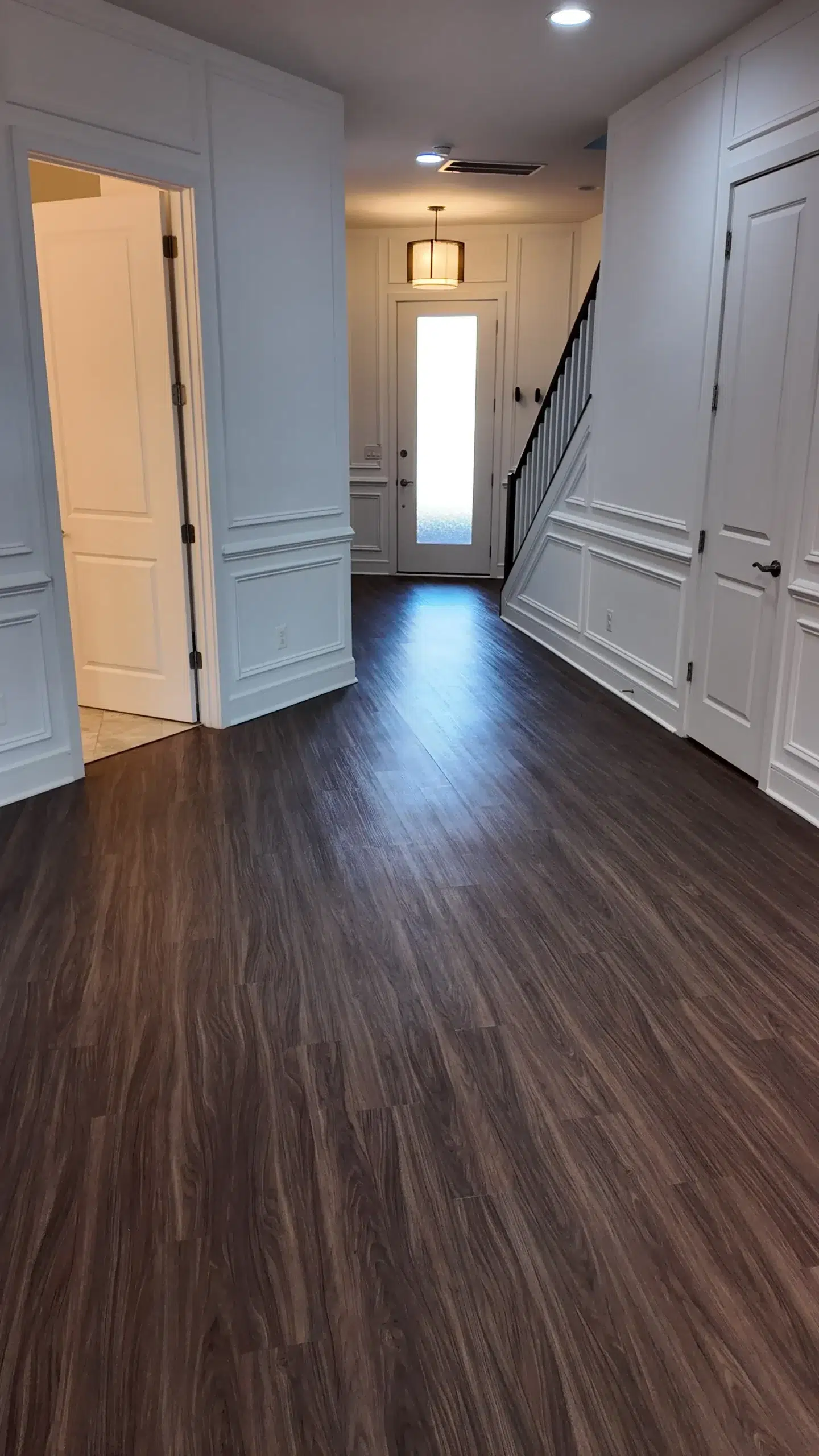 Freshly Painted White Hallway and Trim in a Modern Home A newly painted white hallway with wainscoting, dark wood floors, and a front door.